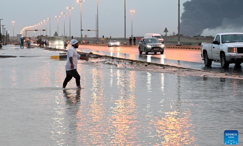 A man crosses a flooded street after heavy rain in Mubarak Al-Kabeer Governorate, Kuwait, March 25, 2026. Heavy rainfall and unstable weather conditions affected several parts of Kuwait on Wednesday. (Photo by Asad/Xinhua)


