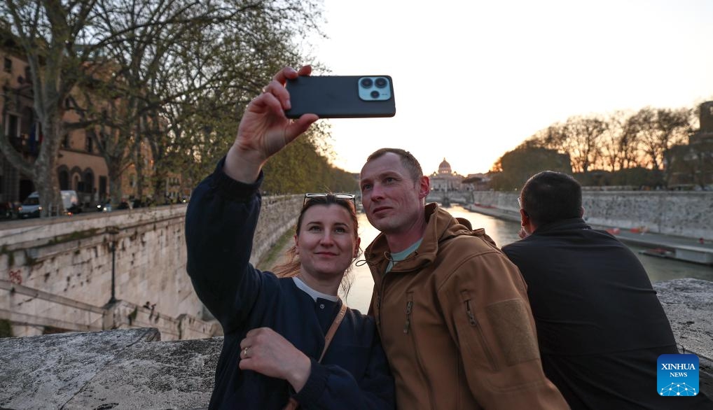 People take selfies along the Tiber River at sunset in Rome, capital of Italy, March 25, 2026. (Xinhua/Wang Kaiyan)

