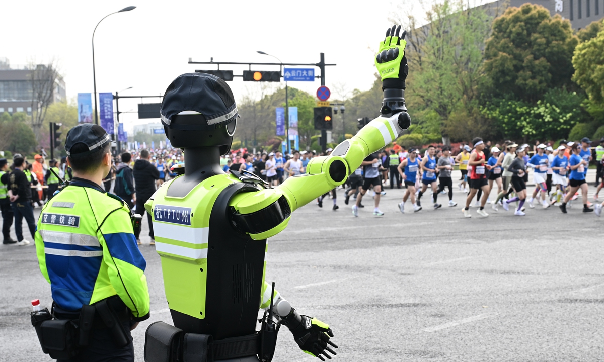 An artificial intelligence (AI) traffic management robot (right) guides marathon runners alongside a traffic police officer in Hangzhou, East China's Zhejiang Province, on March 29, 2026. On that day, a half-marathon kicked off in the city. Local public security authorities introduced AI traffic management robots, augmented reality glasses, and other equipment to safeguard the event with technological power. Photo: VCG
