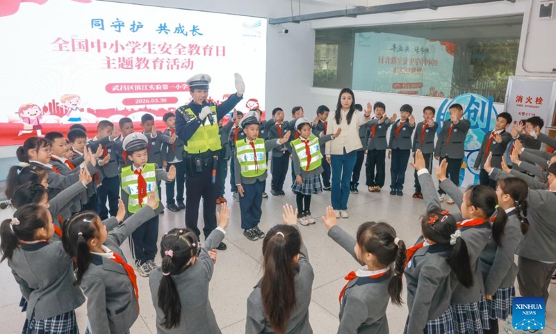 A traffic police guides pupils in doing gesture exercises of traffic safety at a primary school in Wuhan City, central China's Hubei Province, March 30, 2026. March 30 marks China's national safety education day for middle and primary school students. (Photo by Zhao Jun/Xinhua)