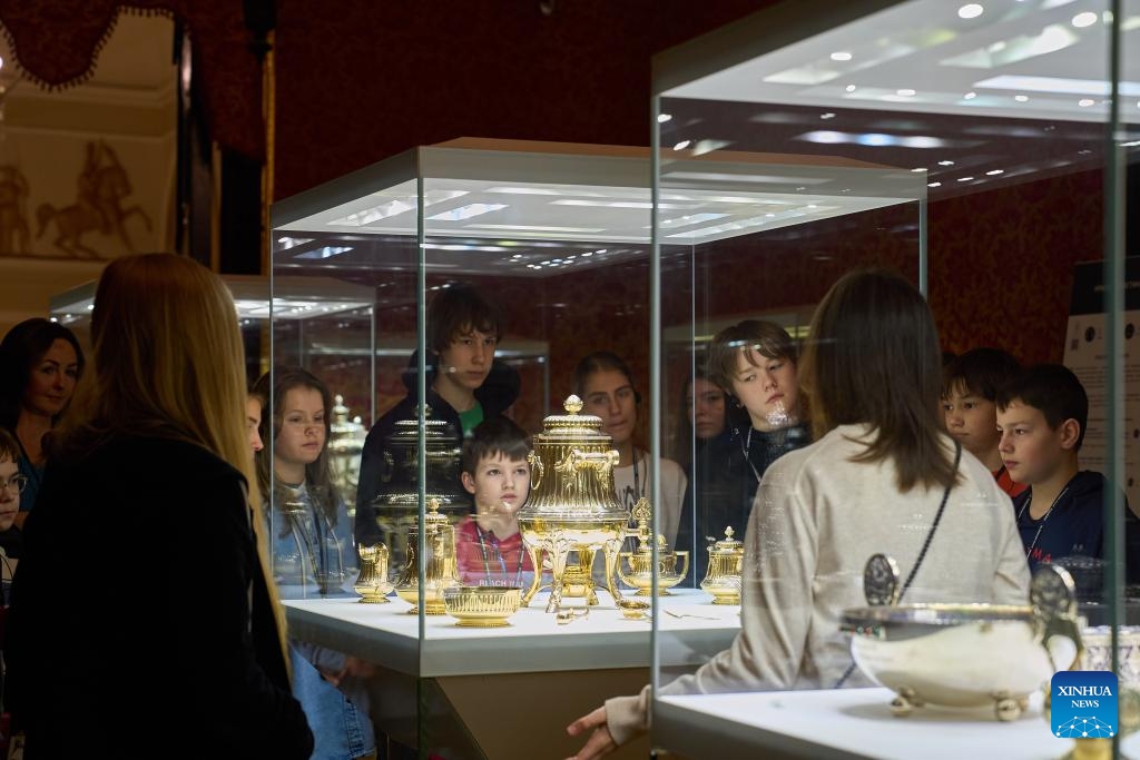 Students view a gilded tea set at Fabergé Museum in St. Petersburg, Russia, on April 7, 2026. The Fabergé Museum boasts a collection of over 4,000 works of art, including gold and silver objects as well as porcelain. Among its most celebrated treasures is a set of nine imperial Easter eggs. (Photo by Guo Feizhou/Xinhua)