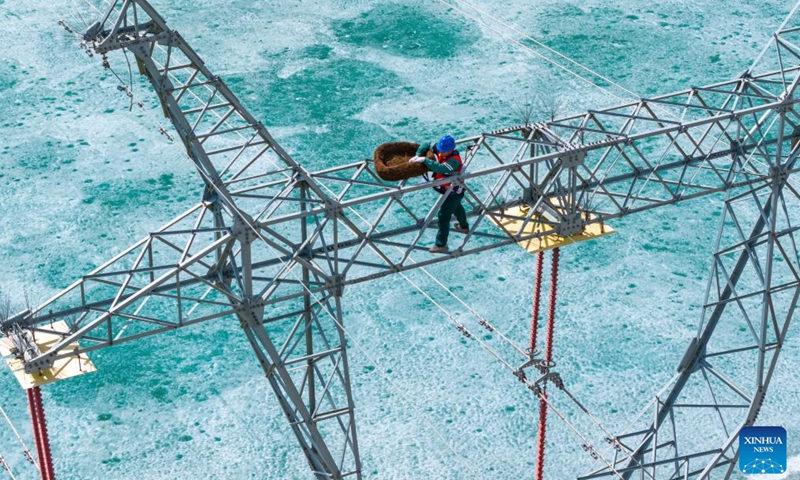 An aerial drone photo taken on April 1, 2026 shows a staff member of the State Grid Altay Power Supply Company installing a bird nest at the Ulunggur Lake National Wetland Park in Fuhai County of Altay Prefecture, northwest China's Xinjiang Uygur Autonomous Region. (Photo by Nurbek Nurman/Xinhua)

