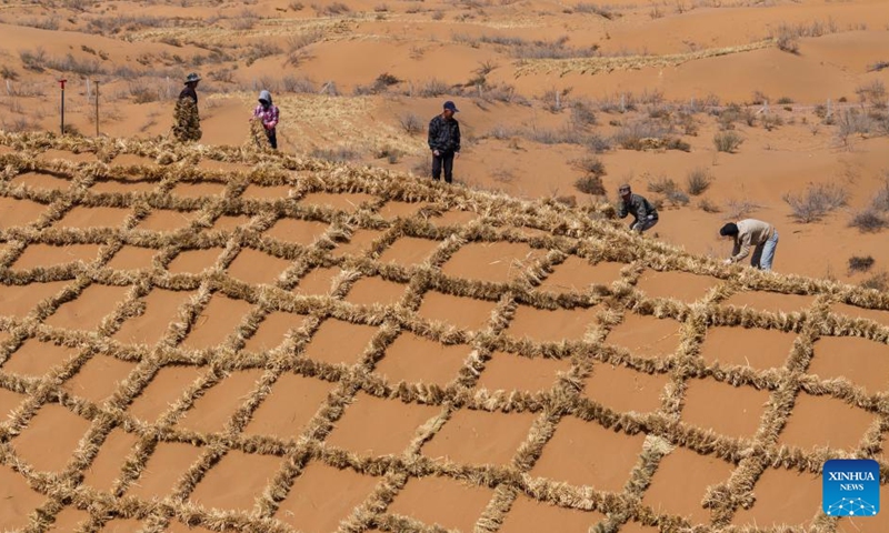 A drone photo taken on April 10, 2026 shows workers paving straw checkerboard barriers on sand in the Tengger Desert, northwest China's Ningxia Hui Autonomous Region. Workers in Zhongwei City are upgrading desert barriers in the Tengger Desert by laying new straw checkerboard barriers to improve desert control efficiency. (Xinhua/Yang Zhisen)