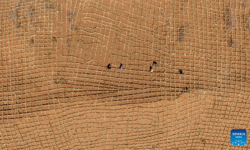 An aerial drone photo taken on April 10, 2026 shows workers paving straw checkerboard barriers on sand in the Tengger Desert, northwest China's Ningxia Hui Autonomous Region. Workers in Zhongwei City are upgrading desert barriers in the Tengger Desert by laying new straw checkerboard barriers to improve desert control efficiency. (Xinhua/Yang Zhisen)