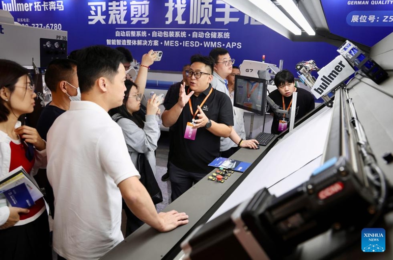 Exhibitors introduce an intelligent cutting machine to visitors during the 28th Straits Textile and Clothing Fair in Shishi, southeast China's Fujian Province, April 18, 2026. The fair kicked off here on Saturday. (Xinhua/Jiang Kehong)