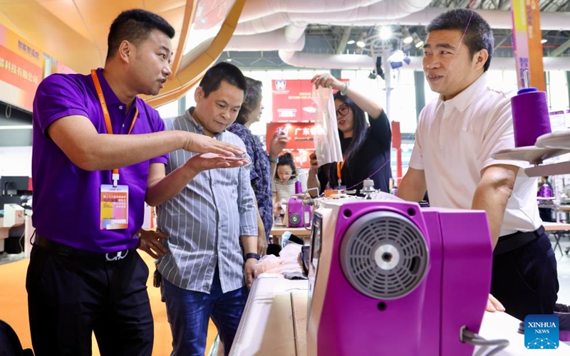 An exhibitor introduces a sewing machine to visitors during the 28th Straits Textile and Clothing Fair in Shishi, southeast China's Fujian Province, April 18, 2026. The fair kicked off here on Saturday. (Xinhua/Jiang Kehong)
