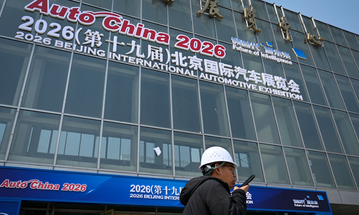 A worker uses his phone while walking past the venue of this year's Beijing Auto Show on the eve of the event at the China International Exhibition Center in Beijing on April 23, 2026. Photo: VCG