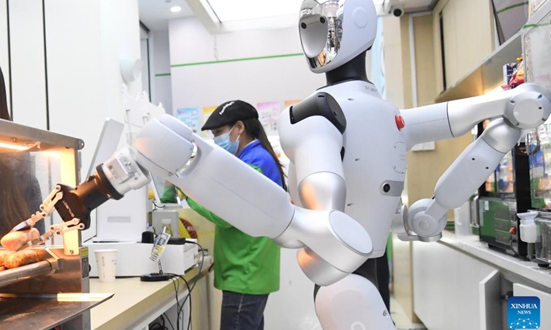 A humanoid robot grabs a grilled sausage at a convenience store in Haidian District of Beijing, capital of China, April 22, 2026. An embodied large model robot has recently been deployed in a convenience store in Haidian District to provide regular service. The robot is responsible for greeting customers, answering product inquiries, providing promotion information, and delivering goods. (Xinhua/Ren Chao)

