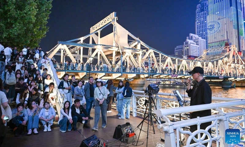 Tourists watch an artist singing by the Haihe River in Tianjin, north China, April 24, 2026. In recent years, Tianjin has become a popular tourist destination, as the city keeps enriching its nighttime experience by expanding tourism scenarios and diversifying business formats. (Xinhua/Sun Fanyue)