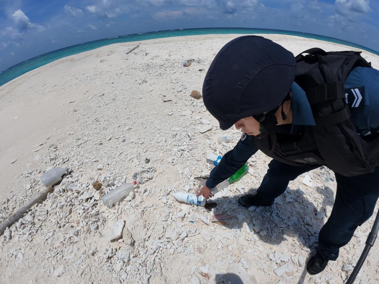 A China Coast Guard officer picks up and inspects a discarded plastic bottle marked with Philippine brand at Tiexian Jiao on May 3, 2026. Photo: CCG