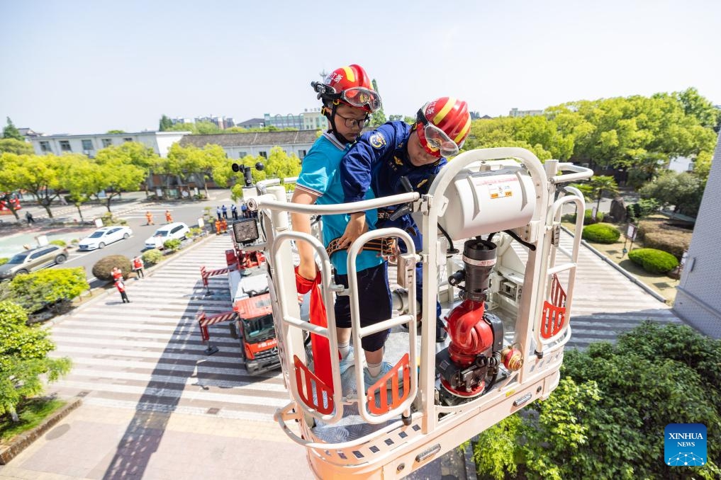 A firefighter uses a ladder truck to rescue a trapped student during an emergency evacuation drill at a primary school in Huzhou City, east China's Zhejiang Province, May 11, 2026. A variety of activities were held across the country marking the upcoming National Disaster Prevention and Reduction Day. (Photo by Yi Fan/Xinhua)
