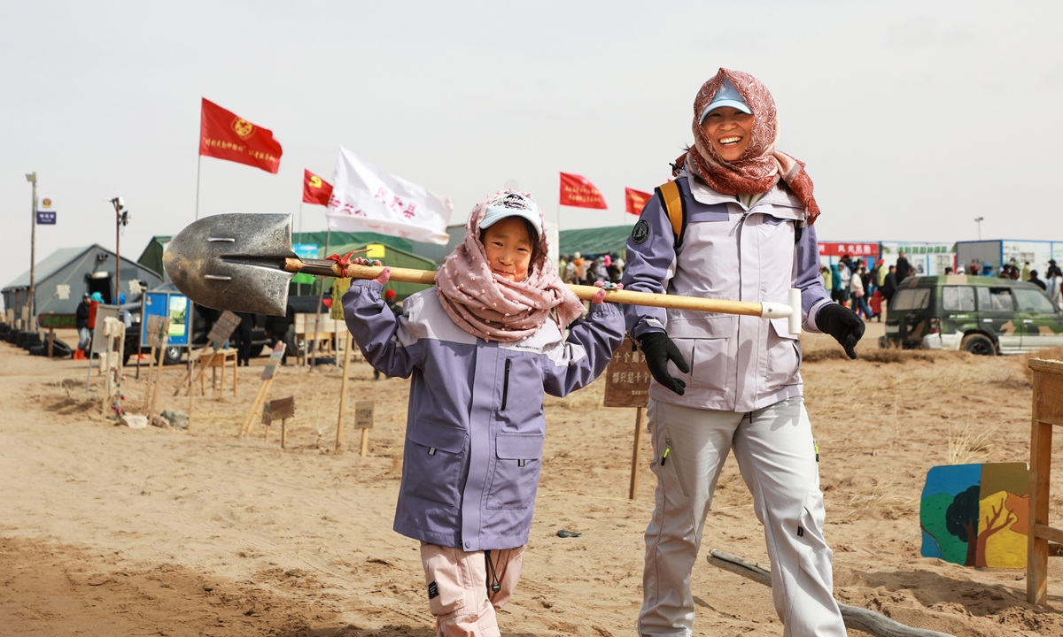 A child and an adult walk together with a shovel, ready to join the reforestation effort in the desert of Minqin County. Photo: Courtesy of publicity department of Minqin County