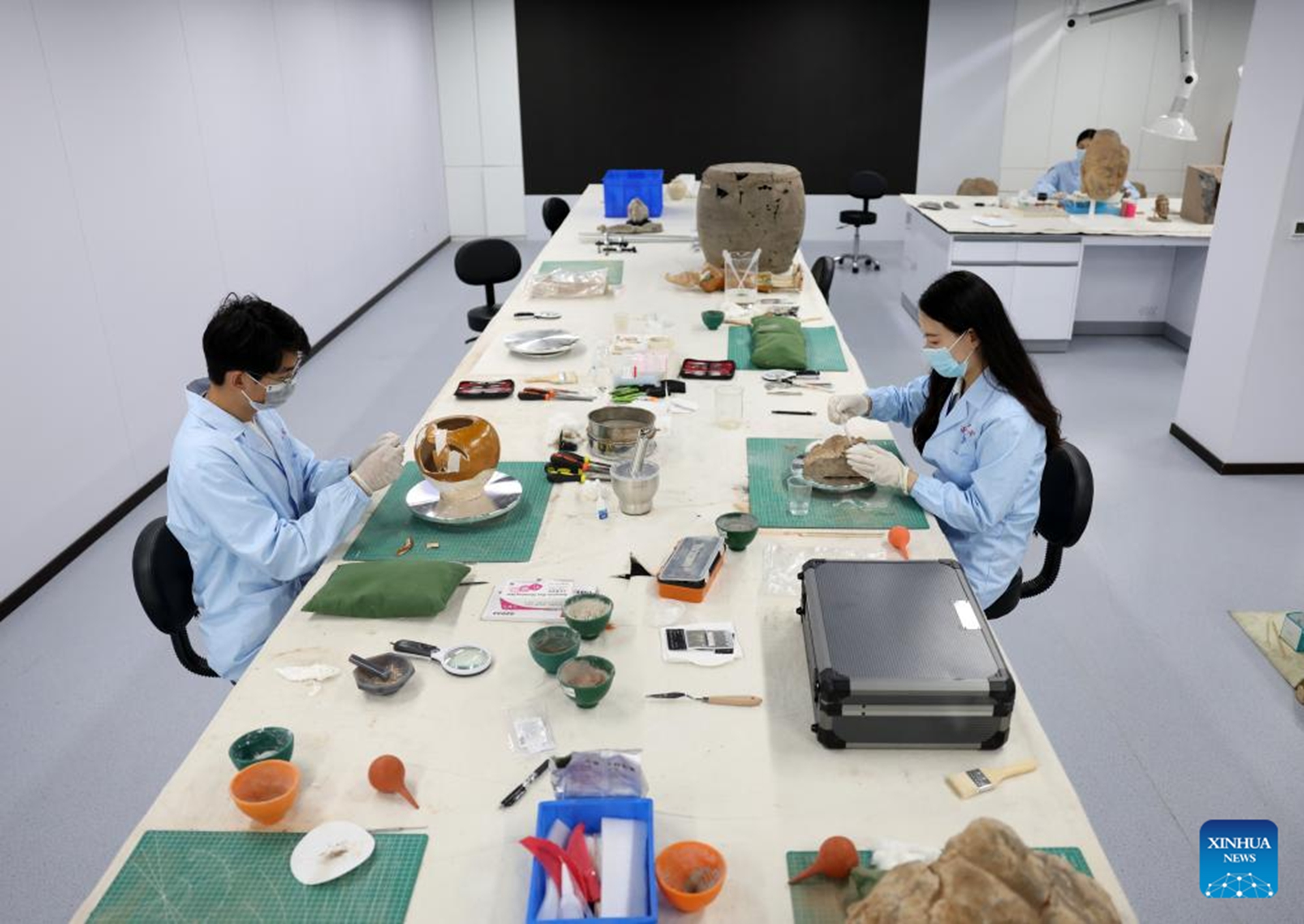 Rui Zihang (L) and Li Peijun, both members of the conservation, research and monitoring team under Longmen Grottoes Academy, restore cultural relics at a conservation center of Longmen Grottoes Academy in Luoyang, central China's Henan Province, May 12, 2026. (Xinhua/Li Jianan)