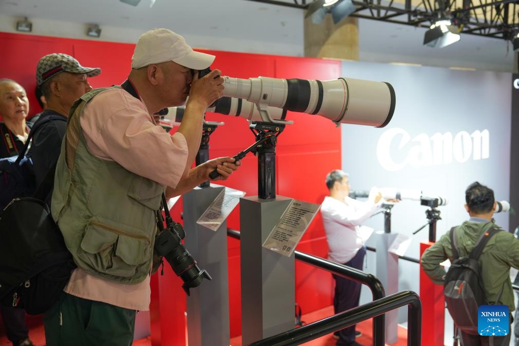 Visitors try telephoto lenses at the exhibition area of Canon at the 27th China International Photograph & Electrical Imaging Machinery and Technology Fair (China P&E) at the Beijing Exhibition Center in Beijing, capital of China, May 18, 2026. The 27th China International Photograph & Electrical Imaging Machinery and Technology Fair (China P&E) concluded here on Monday. With an exhibition area of more than 20,000 square meters, the event gathered more than 120 exhibitors, covering a full range of imaging gear including camera, lens, lighting equipment, storage device and others. (Photo: Xinhua)