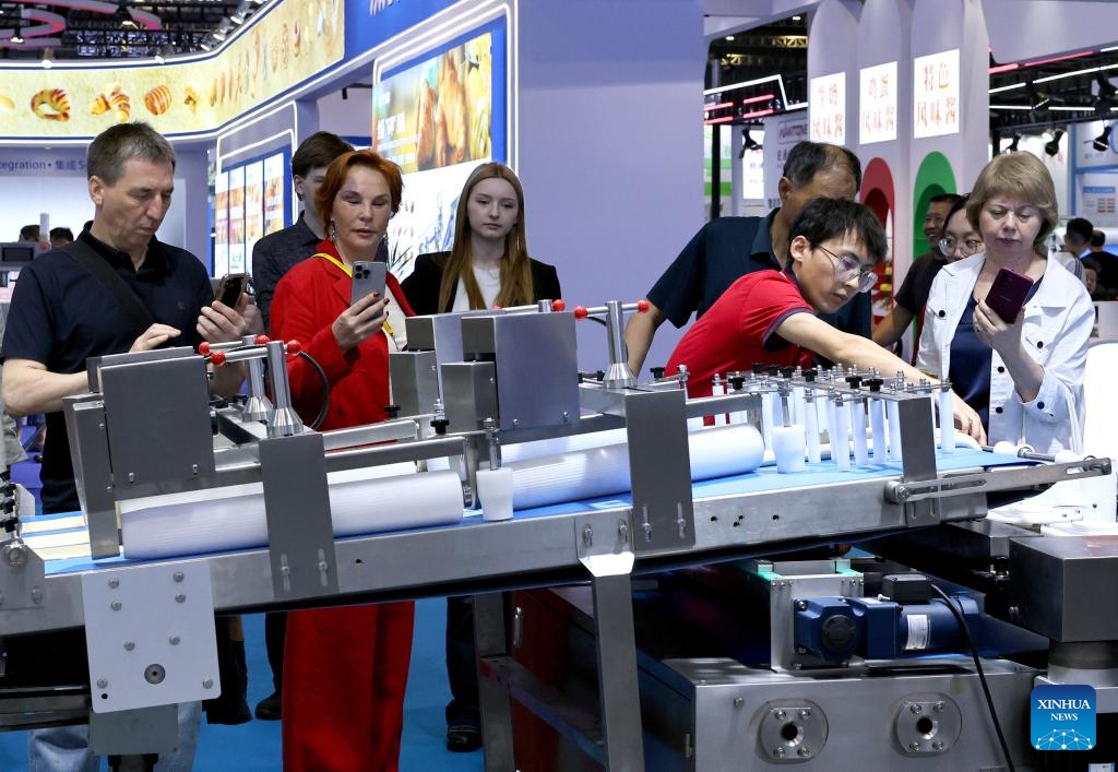 Foreign merchants take pictures in front of a food production assembly line during Bakery China 2026 at National Exhibition and Convention Center in Shanghai, east China, May 20, 2026. Bakery China 2026 opened here on Wednesday. Covering 330,000 square meters show space, the exhibition attracts over 2,200 exhibitors from more than 70 countries and regions, showcasing the whole industry chain products of the baking industry, from raw materials, technical equipment to integrated solutions. (Photo: Xinhua)