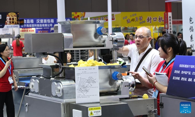 A foreign merchant talks with a staff member in front of a filling machine during Bakery China 2026 at National Exhibition and Convention Center in Shanghai, east China, May 20, 2026. Bakery China 2026 opened here on Wednesday. Covering 330,000 square meters show space, the exhibition attracts over 2,200 exhibitors from more than 70 countries and regions, showcasing the whole industry chain products of the baking industry, from raw materials, technical equipment to integrated solutions. (Photo: Xinhua)