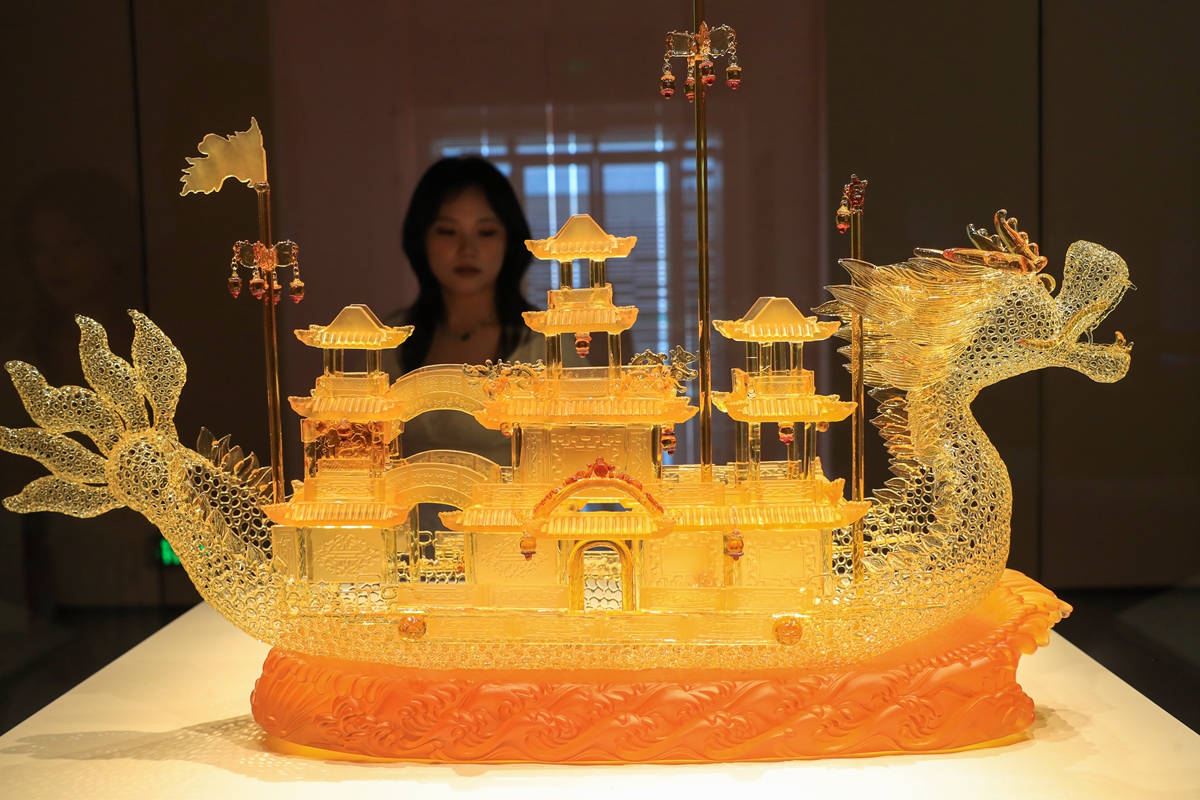 A visitor observes a Liuli (colored glass art) replica of a Sui Dynasty (581-618) dragon boat at the China Grand Canal Museum in Yangzhou, East China's Jiangsu Province, on May 20, 2026. A total of 162 fine glass treasures from ancient and modern times are being displayed in an ongoing exhibition at the museum, showcasing classic inherited glass works as well as contemporary creations.