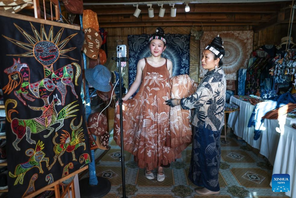 A host (L) introduces a dress made with wax dyeing craft through a livestream in Paimo Village, Danzhai County of southwest China's Guizhou Province, May 20, 2026. Miao wax dyeing, a craft inherited through generations among the Miao ethnic group in southwest China's Guizhou, was listed as a national intangible cultural heritage in 2006. The folk artwork is famous for its elegant color, graceful patterns and rich cultural expressions. (Photo: Xinhua)
