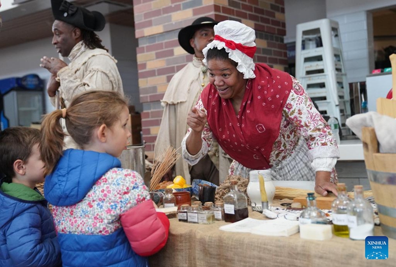 A woman in costumes introduces daily items to children during the Re-enactment Village event in Long Island of New York, the United States, on May 23, 2026. An event titled the Re-enactment Village kicked off in New York on Saturday to recreate the daily life of 18th-century. (Xinhua/Zhang Fengguo)