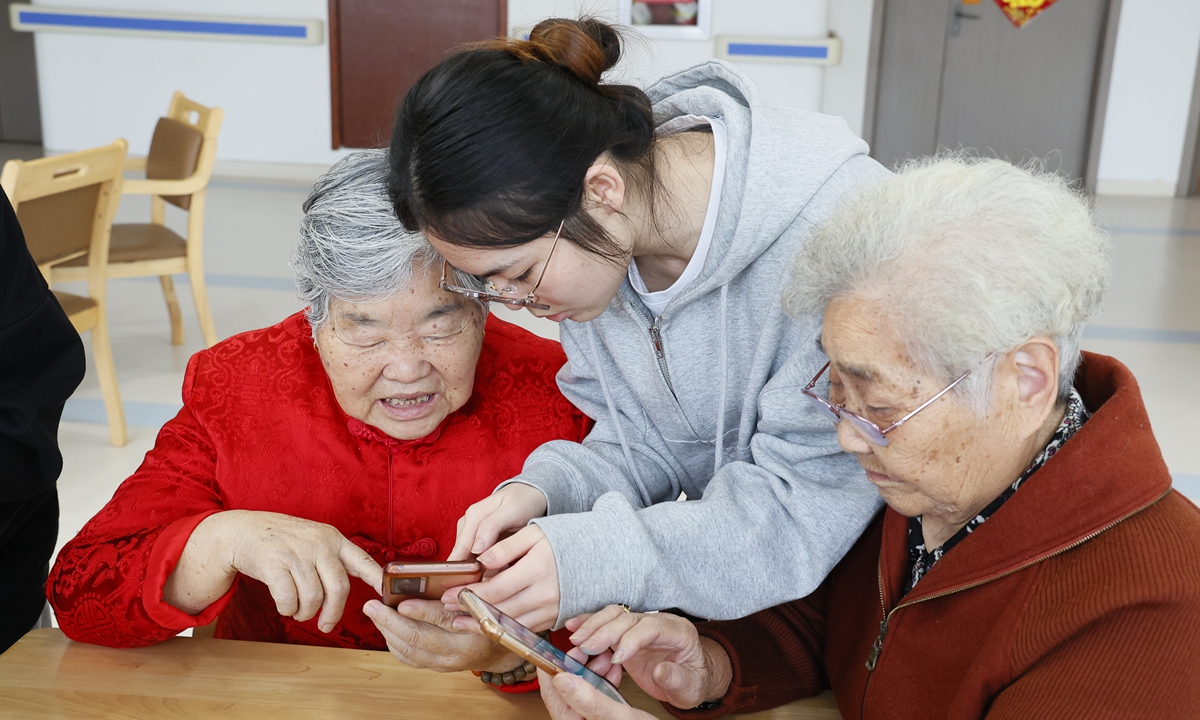 A young person who resides with the elderly at Jinhua social welfare center, East China's Zhejiang Province, teaches senior residents how to use a smartphone on October 23, 2025. Photo: VCG