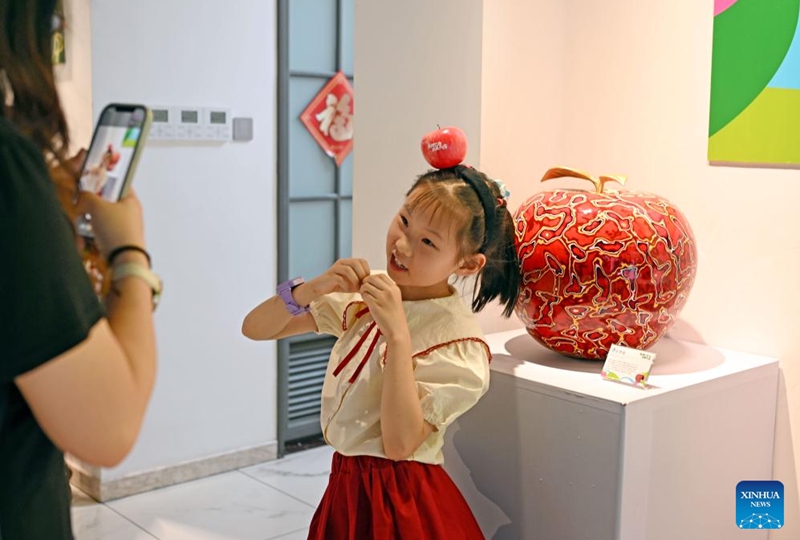 A girl poses for a photo with a copper carving artwork during a pop-up art show titled Zhu Bingren's fruit party in Shanghai, east China, May 30, 2026. The show will last until June 29. (Xinhua/Liu Ying)