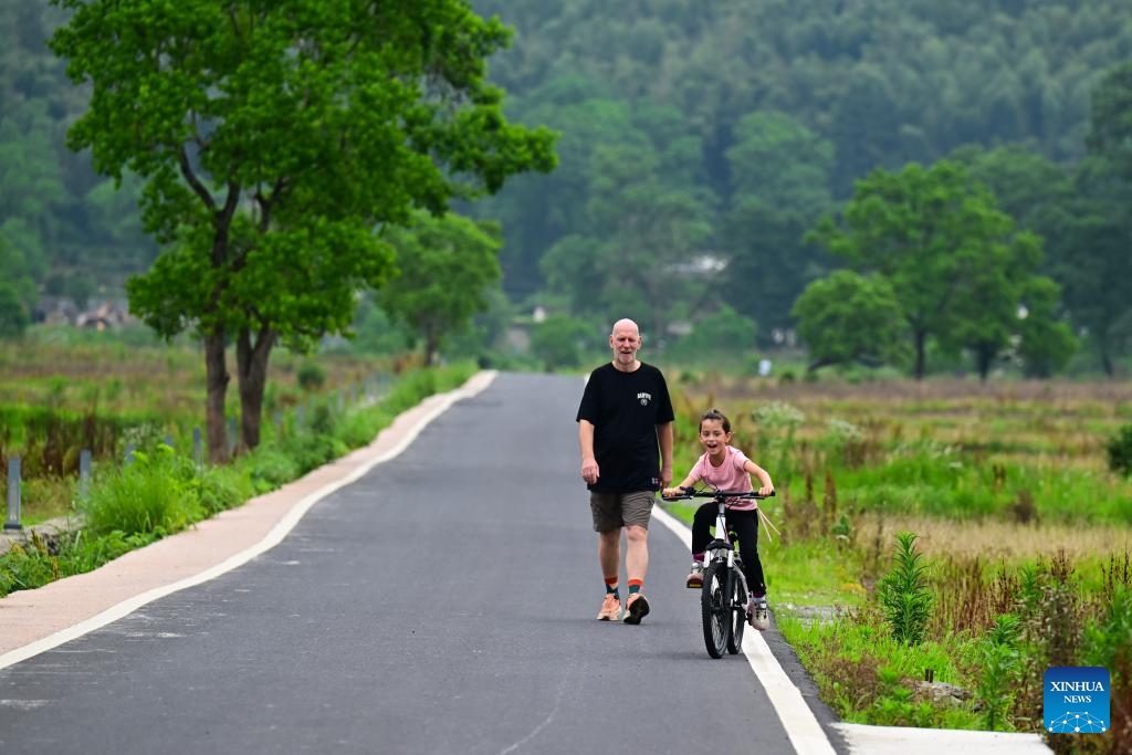 Alina rides a bike accompanied by her father in Yixian County, east China's Anhui Province, on May 29, 2026. When some mayors and city representatives from around the world visited Yixian County for an international event, 8-year-old Alina, who received these foreign guests with her parents, quickly caught people's attention. Fluent in both Chinese and English, she welcomed the guests with a lively performance of Chinese martial arts and Huangmei Opera, earning warm applause. (Photo: Xinhua)