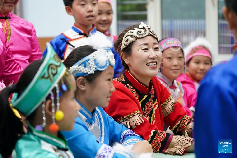 Wu Jing (C), a municipal-level inheritor of Hezhen Yimakan storytelling, teaches students to perform this art at a primary school in Tongjiang City, northeast China's Heilongjiang Province, June 2, 2026. Tongjiang City, home to one of the largest Hezhe communities in China, has stepped up efforts in recent years to safeguard intangible cultural heritage of Hezhe people, including Hezhen Yimakan storytelling, fish-skin craftsmanship, and local fishing and hunting customs. Such efforts aim to help the traditional ethnic culture thrive in modern times. (Photo: Xinhua)