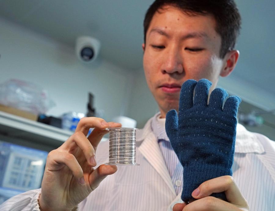 A researcher displays rolled-up fiber chips and a smart tactile glove made by weaving the chips into textiles at Fudan University in east China's Shanghai, Jan. 19, 2026. (Xinhua/Liu Ying)