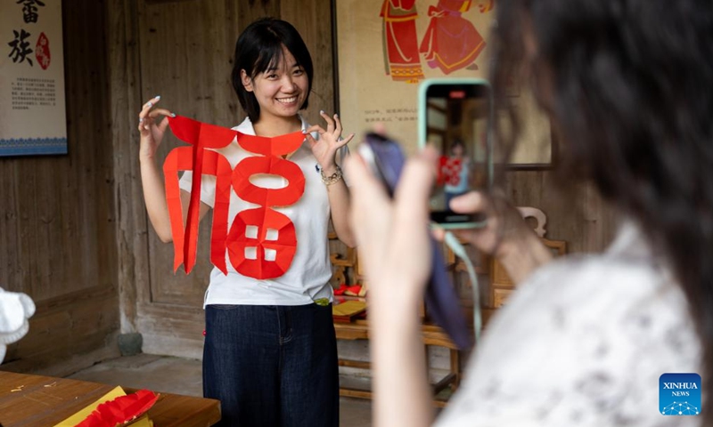 A podcaster presents a She-style paper-cutting work in Banyueli Village of Xiapu County, Ningde City, southeast China's Fujian Province, June 10, 2026. Banyueli, an ancient village of She ethnic group, retains a cluster of well-preserved She-style houses and has several items of intangible cultural heritage. In recent years, local authorities have stepped up efforts to protect and revitalize the ancient village by promoting intangible cultural heritage and integrating cultural resources into tourism development. These efforts have attracted visitors from home and abroad, and helped protect and pass on the cultural legacy of the She ethnic group. (Photo: Xinhua)