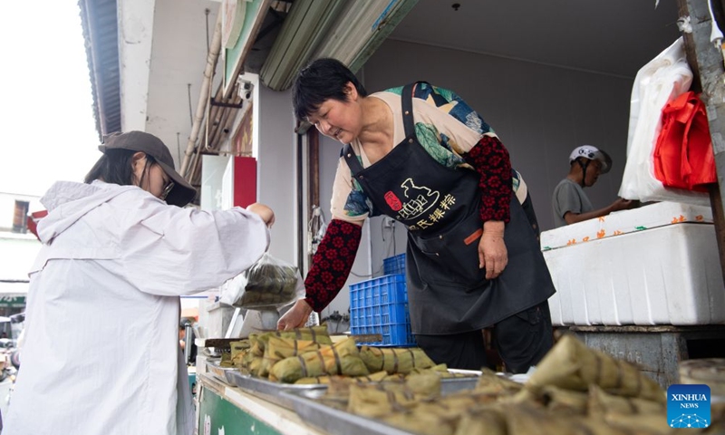 A woman from Shiren Village sells zongzi to a customer at her shop in Xiuning County, Huangshan City of east China's Anhui Province, June 16, 2026. Shiren Village, dubbed the hometown of zongzi (sticky rice dumplings) in ancient Huizhou, boasts a long tradition of zongzi making. The annual sales of zongzi in the village has reached 900,000 yuan (about 133,000 U.S. dollars).(Xinhua/Zhang Duan)