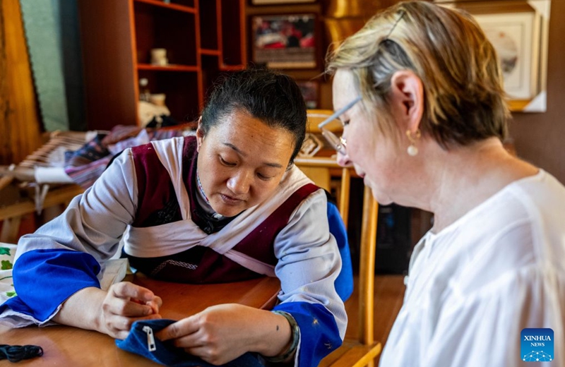 An embroiderer of the Naxi ethnic group (L) explains embroidery work to a foreign tourist at Baisha ancient town in Lijiang, southwest China's Yunnan Province, June 17, 2026. In recent years, Baisha ancient town has drawn on its historical legacy and rich ethnic cultural resources to advance the preservation, transmission and innovative development of the embroidery of the Naxi ethnic group, injecting new vitality into the ancient craft. Photo: Xinhua