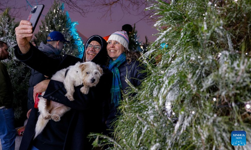 People and their pet dog pose for selfies behind a decorated Christmas tree during the July Christmas event in Canberra, Australia, July 4, 2026. July Christmas stems from Australians' longing for a traditional white Christmas in the Southern Hemisphere. (Photo by Chu Chen/Xinhua)