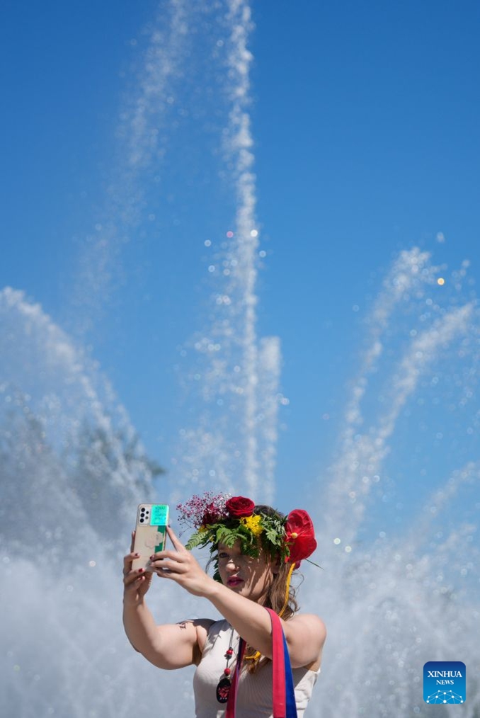 A woman wearing a wreath takes a selfie during the Wianki Festival celebration in Warsaw, Poland, June 20, 2026. The event is an important Polish folk celebration of the summer solstice, during which people carry on ancient customs with wreaths, music and riverside gatherings. (Photo by Jaap Arriens/Xinhua)

