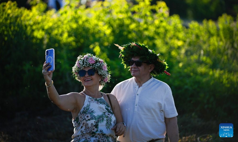 People wearing wreaths take a selfie during the Wianki Festival celebration in Warsaw, Poland, June 20, 2026. The event is an important Polish folk celebration of the summer solstice, during which people carry on ancient customs with wreaths, music and riverside gatherings. (Photo by Jaap Arriens/Xinhua)

