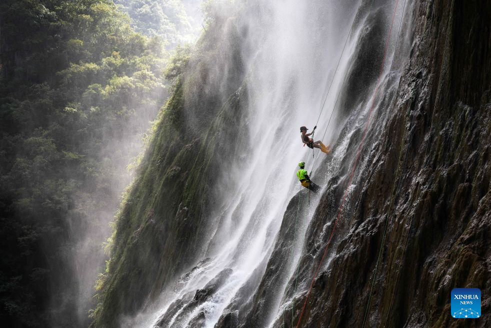 A tourist experiences waterfall rappelling under the guidance of a staff member at a scenic area in Huangping County, Qiandongnan Miao and Dong Autonomous Prefecture, southwest China's Guizhou Province, July 29, 2026. The waterfall rappelling here has attracted tourists for cool relief and exhilarating experience. (Xinhua/Yang Wenbin)