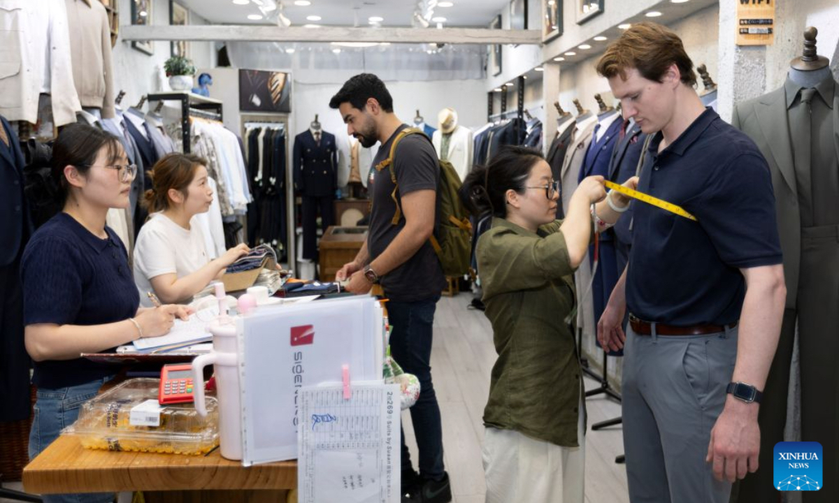 A tourist from the United States gets measured for custom-made suits at a clothing store in Shanghai, east China, July 22, 2026. The foreign visitors entering Shanghai increased 22 percent year on year in the first half of 2026, thanks to the country's expanding visa exemption policies. Chinese designer products have emerged as a new driver of inbound consumption. Rather than buying only traditional Chinese specialties such as tea and silk, overseas visitors are increasingly following shopping tips on social media to seek out bags, footwear, clothing and other products by Chinese designers. (Xinhua/Wang Xiang)