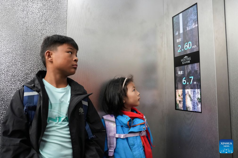 Students look at a screen showing the speed and height of a cliff elevator at Nizhu River Grand Canyon in Puli Township, Xuanwei City, southwest China's Yunnan Province, Aug. 30, 2026. Nizhuhe Village is located at the bottom of the Nizhu River Grand Canyon in southwest China's Yunnan Province. What separates Nizhuhe Village and the Guanzhai primary school on the mountain top is a vertical drop of over 500 meters. Students living at the canyon bottom used to take nearly half a day to travel from home to school.
In 2022, significant changes in the means of local commuting took place upon the completion and opening of the Nizhu River Grand Canyon scenic area, which came with a 268-meter-high cliff elevator and a cable car system that were available to local villagers, including students, free of charge.
Today, the combination of sightseeing shuttle vehicles, elevators and cable cars has shortened students' journey to school to about 30 minutes. A dedicated passage has also been set up for them, with police officers and dedicated staff members deployed along the commuting route. (Xinhua/Chen Xinbo)