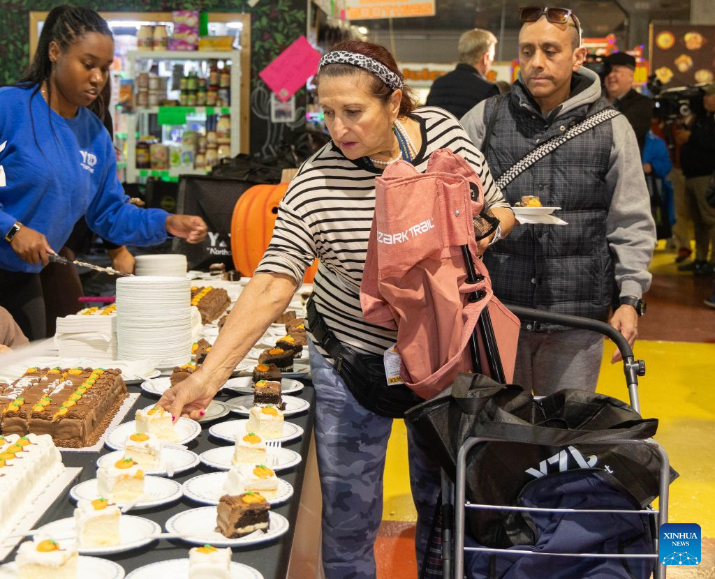 A woman picks up a free cake slice at a farmers' market during the Thanksgiving Turkey Drive in Toronto, Canada, on Oct. 11, 2026. The annual event took place here on Sunday, providing 300 free turkeys for residents in need ahead of Canada's Thanksgiving Day, which falls on the second Monday of October each year. (Photo by Zou Zheng/Xinhua)