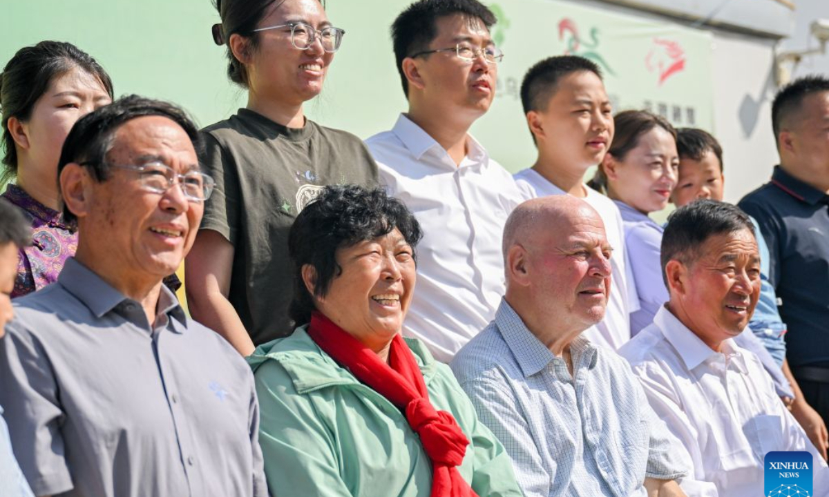 Ronald Sakolsky (2nd R, front) poses for a group photo with Yin Yuzhen (2nd L, front) and her relatives and friends in the Maowusu Sandy Land in north China's Inner Mongolia Autonomous Region, Aug. 25, 2026. Twenty-six years had passed before Yin Yuzhen, a national-honored sand-control villager in China's Inner Mongolia, finally sat down to have a reunion feast with her American friend Ronald Sakolsky.
The story behind the feast began in 1999, when Sakolsky taught English at a school in central China's Henan Province under a teachers' exchange program between the two countries.
By then, Yin had spent more than a decade battling desertification that had severely threatened her livelihood, even half burying her house during sandstorms.
After watching a television news report featuring Yin's tireless work, he was deeply moved and raised 5,000 U.S. dollars to help Yin in her afforestation efforts against desertification.
The saplings bought and planted with that donation have since grown into a forest of more than 50,000 towering trees.
As Sakolsky left Yin's home after their reunion in Maowusu Sandy Land on Tuesday, Yin presented him with gifts she had long prepared. (Xinhua/Lian Zhen)
