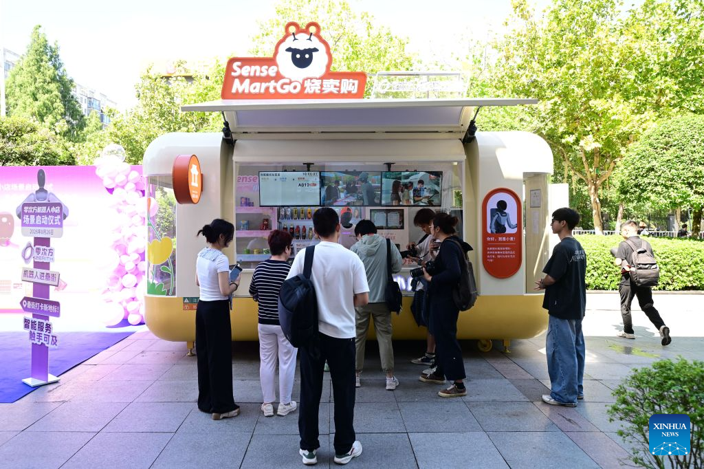People shop at an embodied intelligence robot store at Leijie Street in Hefei, east China's Anhui Province, Aug. 26, 2026. Four embodied intelligence robot stores equipped with wheeled humanoid robot shop assistants have officially opened in several cultural, tourism and commercial blocks in Hefei. The robot shop assistants are able to automatically recognize, grab and deliver merchandise to customers. (Xinhua/Zhou Mu)