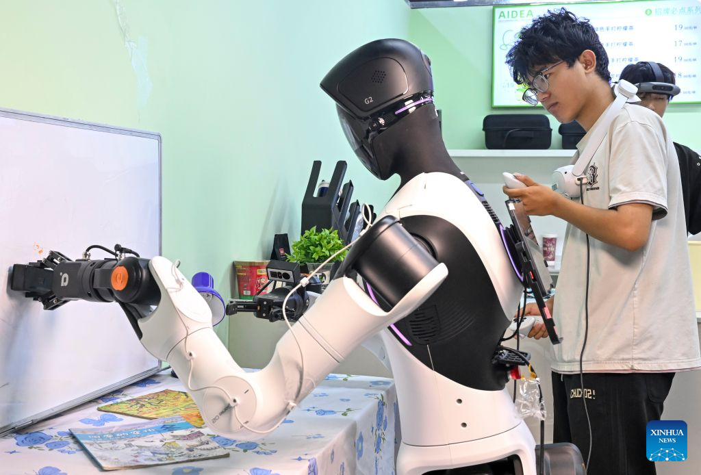 A staff member trains a robot to clean a whiteboard at Maniformer, a physical AI data service platform, in Shanghai, east China, Aug. 5, 2026. In Shanghai's tech companies like AGIBOT and Maniformer, embodied intelligence robots are trained in household, retail, sorting, production and other real-world scenarios, to advance their AI capabilities for real-life use. (Xinhua/Chen Haoming)