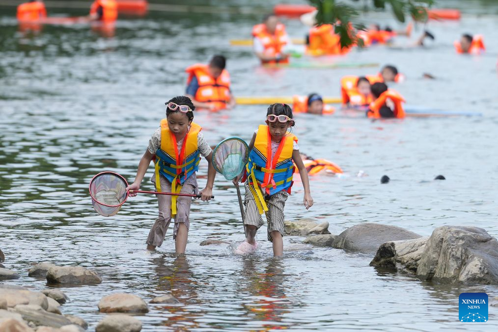 Children catch fish in a stream in Anji County, east China's Zhejiang Province, Aug. 6, 2026. During the summer vacation, Anji County leverages its cool weather and beautiful scenery, attracting numerous tourists to escape the summer heat. (Xinhua/Huang Zongzhi)