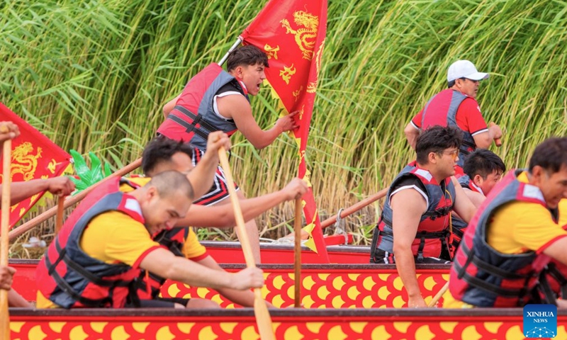 Anwar Kurban (L top) and his teammates compete during a trial match of the 2026 dragon boat race on Hongyan River in Korla City, northwest China's Xinjiang Uygur Autonomous Region, June 19, 2026. (Photo by Ai Houwei/Xinhua)
