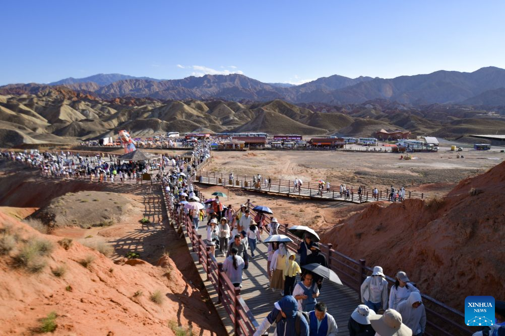 Tourists visit the Zhangye Danxia Scenic Area, renowned for its Danxia landforms featuring striking red sandstone formations, in Zhangye, northwest China's Gansu Province, Aug. 4, 2026. The scenic area in Gansu has entered its peak tourism season since August, with the average daily number of visitors surpassing 25,000. (Xinhua/Liu Keying)