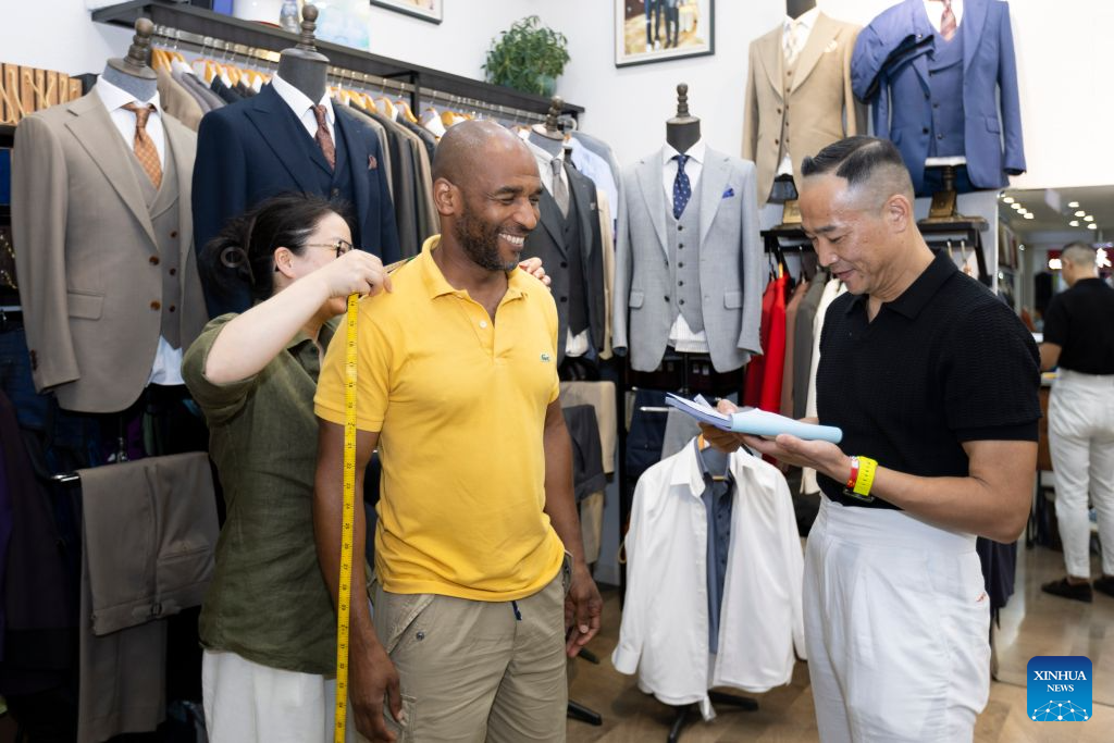 A staff member takes measurements for Martial, a tourist from France, at a clothing store in Shanghai, east China, July 22, 2026. The foreign visitors entering Shanghai increased 22 percent year on year in the first half of 2026, thanks to the country's expanding visa exemption policies. Chinese designer products have emerged as a new driver of inbound consumption. Rather than buying only traditional Chinese specialties such as tea and silk, overseas visitors are increasingly following shopping tips on social media to seek out bags, footwear, clothing and other products by Chinese designers. (Xinhua/Wang Xiang)