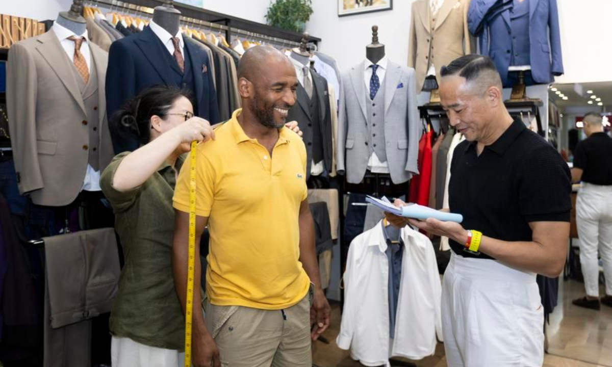 A staff member takes measurements for Martial (C), a tourist from France, at a clothing store in Shanghai, east China, July 22, 2026. (Xinhua/Wang Xiang)