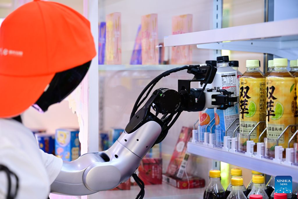 A robot grabs a bottle of electrolyte water from the shelf at an embodied intelligence robot store at Leijie Street in Hefei, east China's Anhui Province, Aug. 26, 2026. Four embodied intelligence robot stores equipped with wheeled humanoid robot shop assistants have officially opened in several cultural, tourism and commercial blocks in Hefei. The robot shop assistants are able to automatically recognize, grab and deliver merchandise to customers. (Xinhua/Zhou Mu)