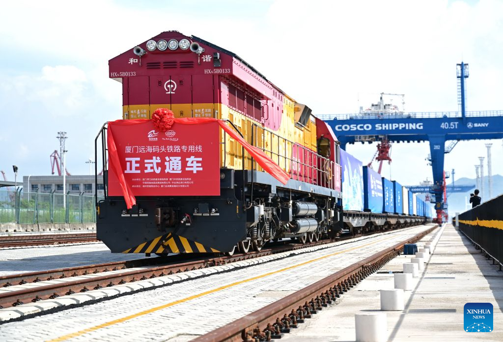 A freight train loaded with containers on a sea-rail intermodal rail line is pictured departing from a quay in Xiamen, southeast China's Fujian Province, July 29, 2026. The sea-rail intermodal rail line is among China's first batch of key projects promoting the integration of transport and logistics. Stretching 1,586 meters, it is designed to handle an annual throughput of 250,000 TEUs of containers and 250,000 tonnes of bulk cargo.
Running perpendicularly to the shoreline and located just 70 meters from the quay apron, the rail line enables cargo to be transferred directly from ships to trains for onward transport. (Xinhua/Lin Shanchuan)