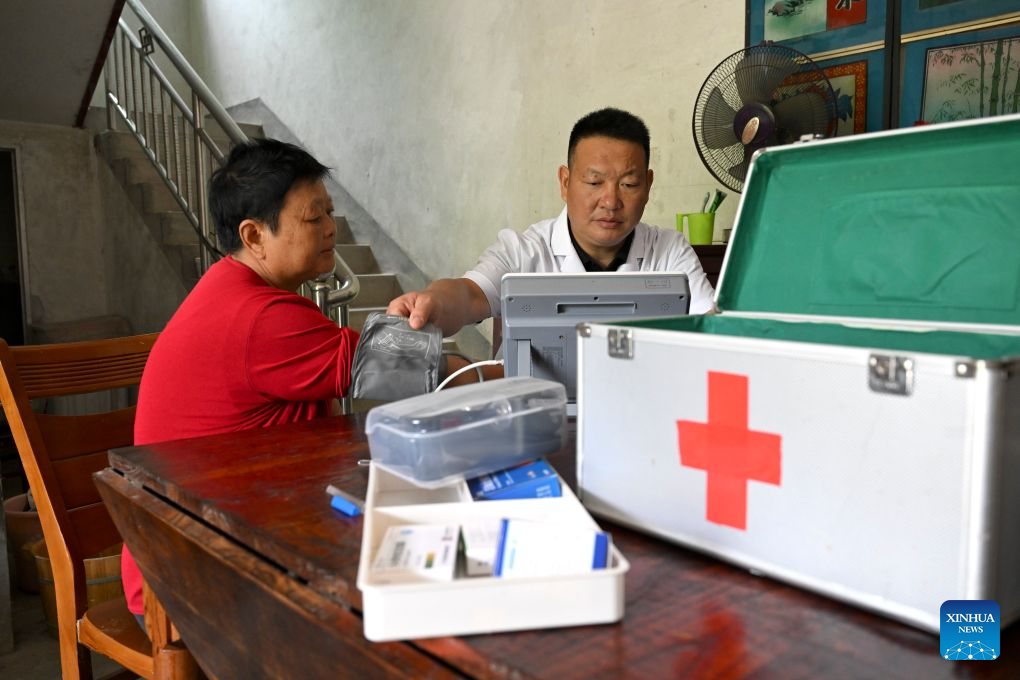 Doctor Yu Jiajun (R) treats villager Wang Jiabi at her home in Qishan Village of Mabu Town, Jinzhai County of Lu'an City, east China's Anhui Province, June 26, 2026. Haidao Village of Qishan Village is located deep in the mountains near the Xianghongdian Reservoir area in Jinzhai County of Lu'an City, east China's Anhui Province. Yu Jiajun, the only village doctor, takes charge of health care for more than 500 villagers there and in the surrounding areas.

In the past, there was no clinic. Villagers had to row a boat for two or three hours to go to the health center in the Mabu Town to see the doctor.

After graduating from a medical school, following his father's last wishes, Yu Jiajun gave up his job in the city and returned to the village where he was born to work as a village doctor in the year of 2000. In order to visit his patients timely, Yu and his wife set up their home on a wooden boat, named Haidao Clinic, and provided medical care to villagers on the boat.

In recent years, many changes have taken place. The clinic was rebuilt in 2019. With the help of the local government, a standardized diagnosis and treatment building was set up on the shore. Yu's work focus has also shifted from emergency treatment in the past to offering medical service for chronic diseases.

However, Yu still need to drive his boat to make visits, as he has been always doing in the past years. Since working as the village doctor, he has changed four boats, conducting more than 20,000 medical consultations at patients' home.

Yu joined the Communist Party of China (CPC) in 2014. As a village doctor, he has been fulfilling his own promise to his father and taking the responsibility as a member of the Communist Party.

As long as people need me, I will keep working here, Yu said. (Xinhua/Huang Bohan)