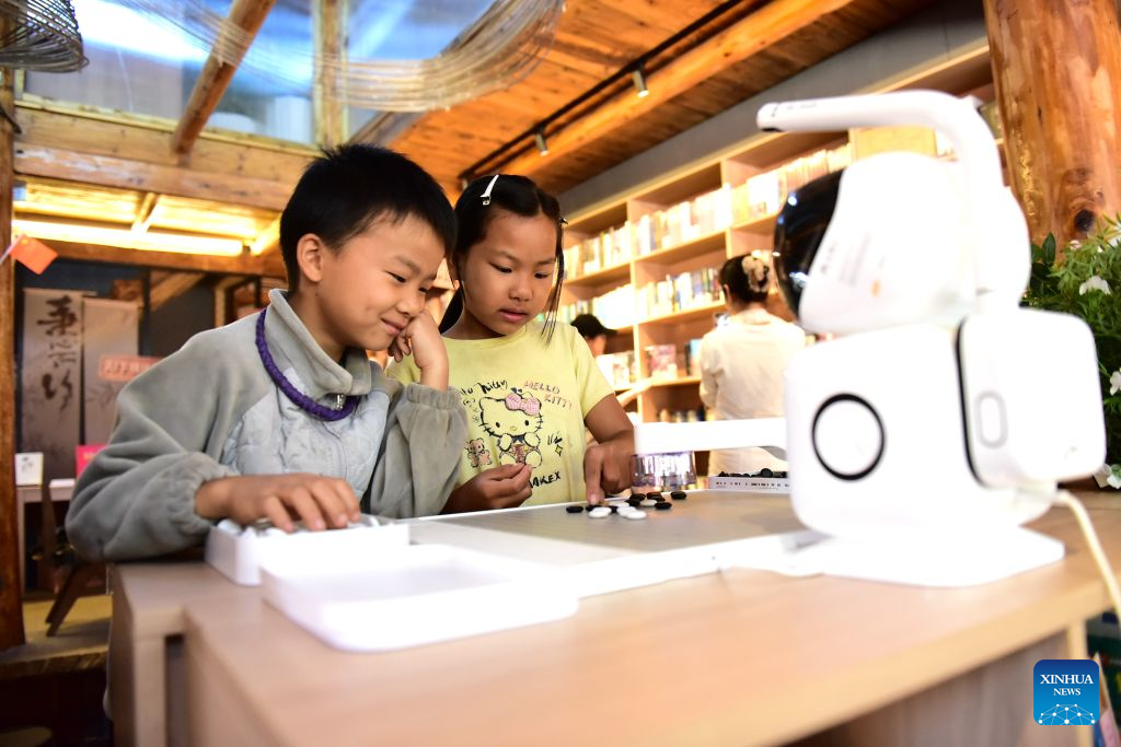 Children play a board game with an AI robot at Basha Village in Congjiang County, southwest China's Guizhou Province, Oct. 6, 2026. Advanced technologies such as exoskeleton devices, AI-powered glasses and robots have enabled diverse and dazzling experiences at tourist destinations across China during the National Day holiday. (Photo by Shi Honghui/Xinhua)